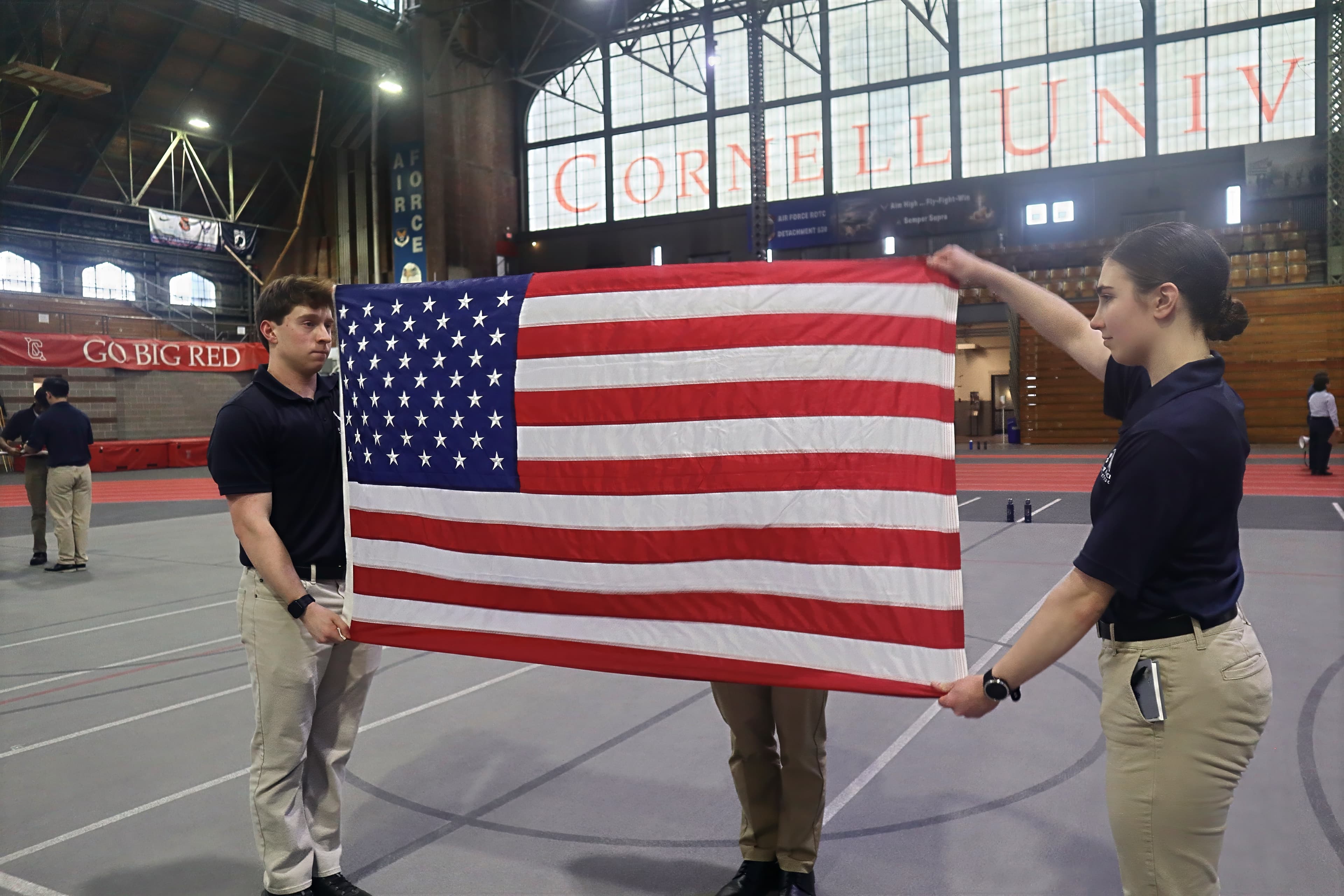 Two Detachment 520 cadets in recruiting polos folding the United States flag on the Barton Hall floor.