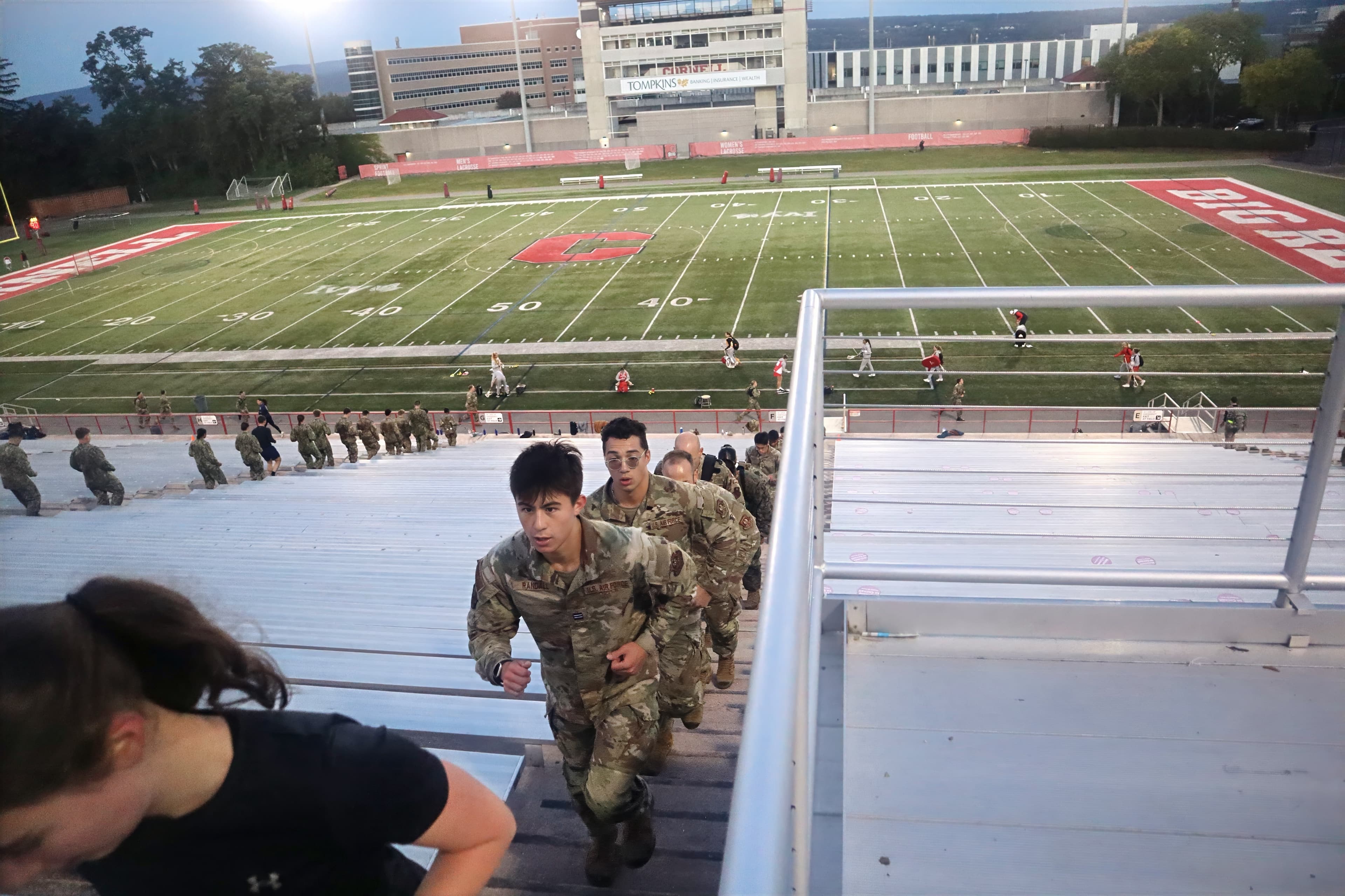 Cadets run up the Schoellkopf Field bleachers at dawn with the stadium and field behind them.