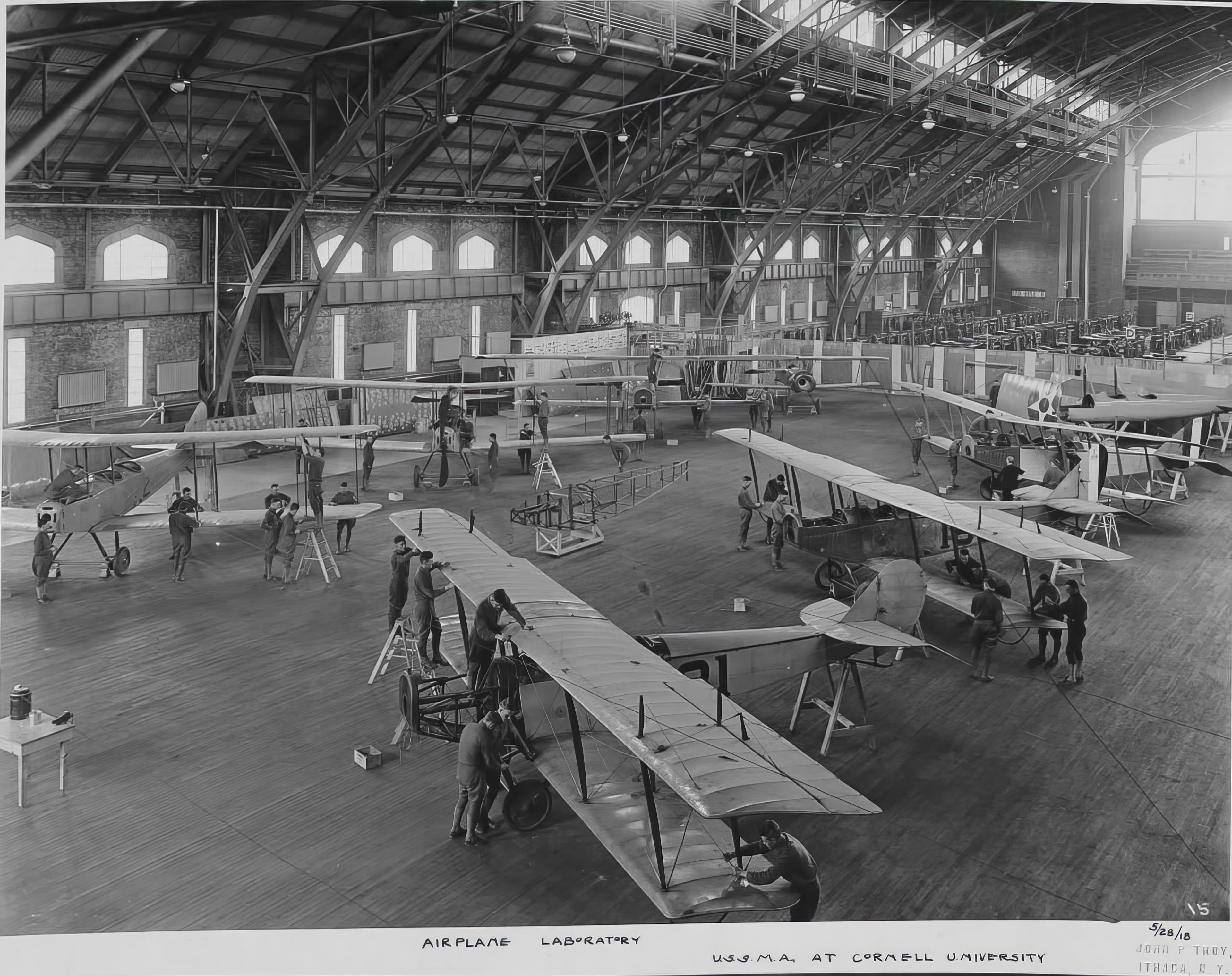 A 1918 photograph captioned Airplane Laboratory, U.S.S.M.A. at Cornell University, showing biplanes and trainees inside the Barton Hall drill deck.