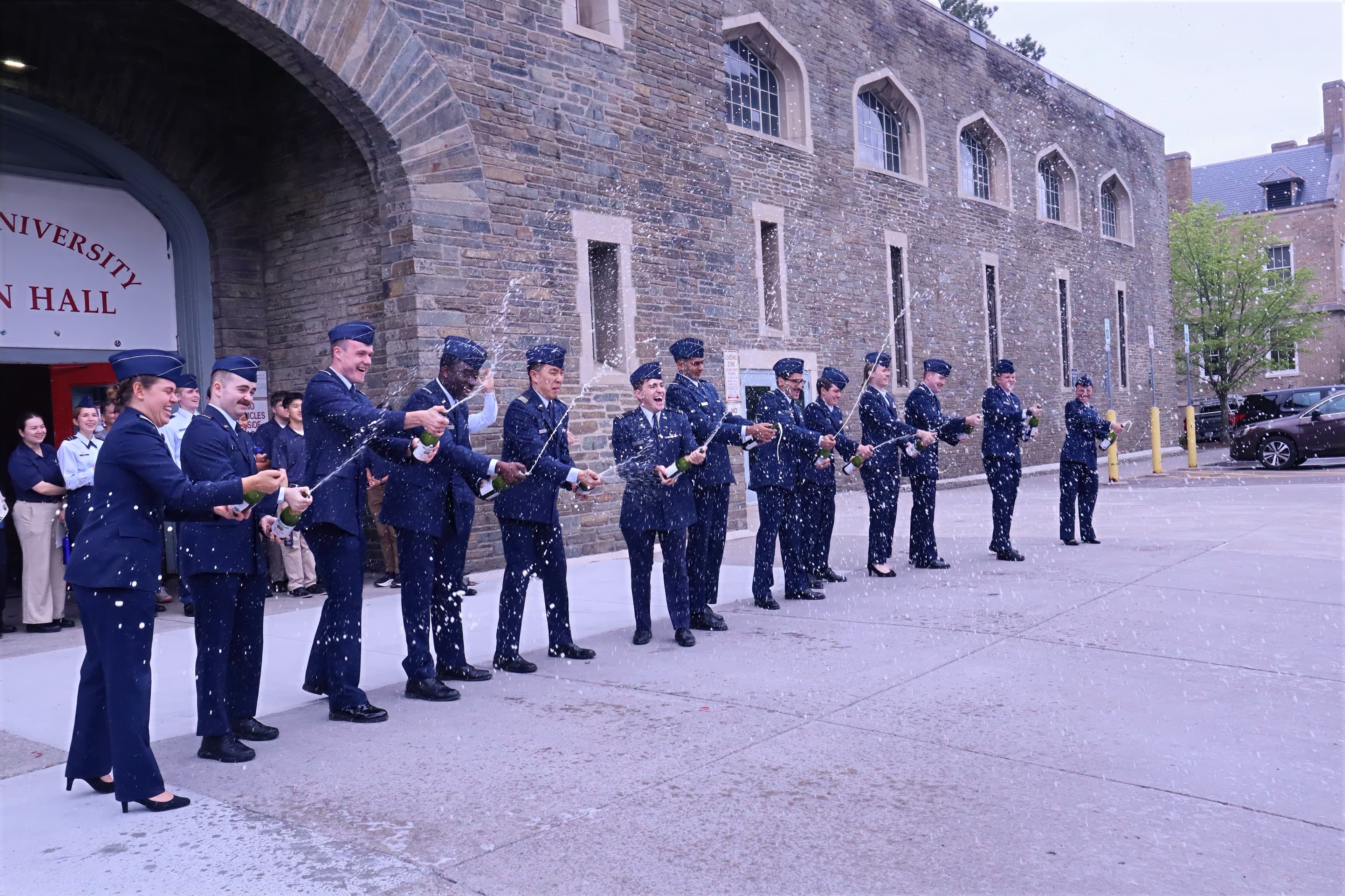 A line of newly commissioned officers in service dress celebrates with champagne outside Barton Hall.