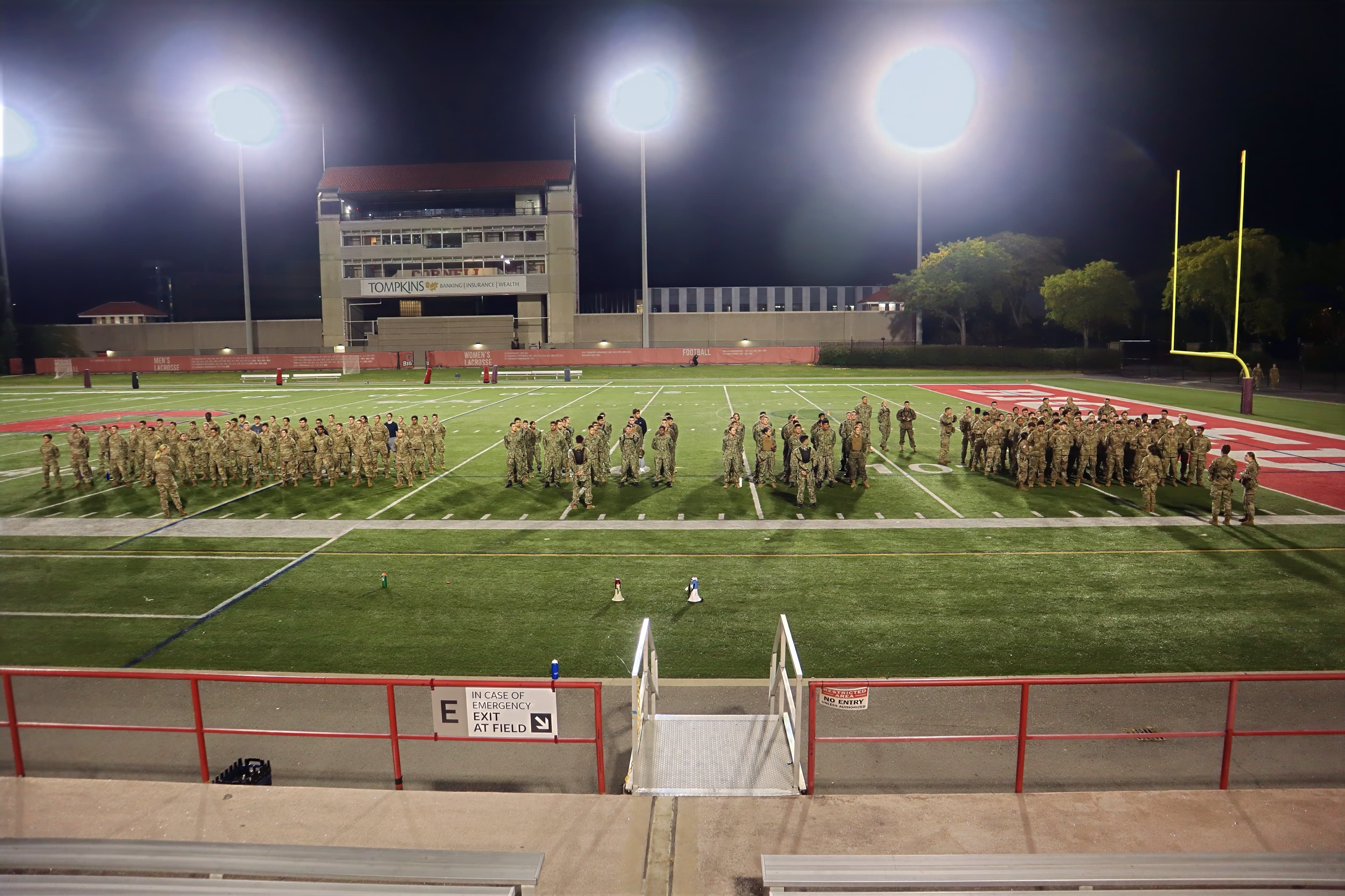 Cadets from multiple services form up on the football field under stadium lights at night for the 9/11 Memorial physical training session.
