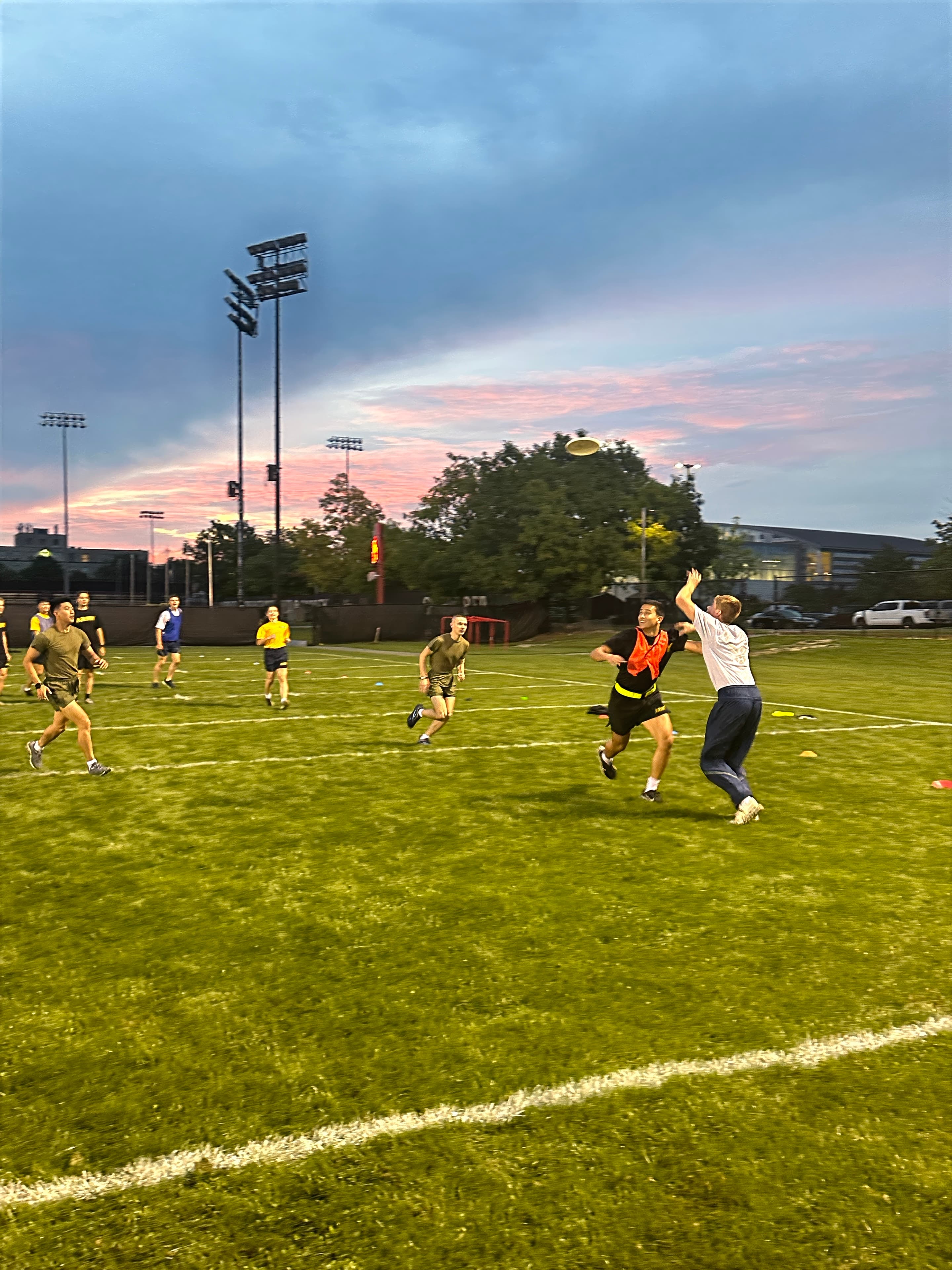Cadets play frisbee on a field at sunset during the Air Force birthday physical training session.
