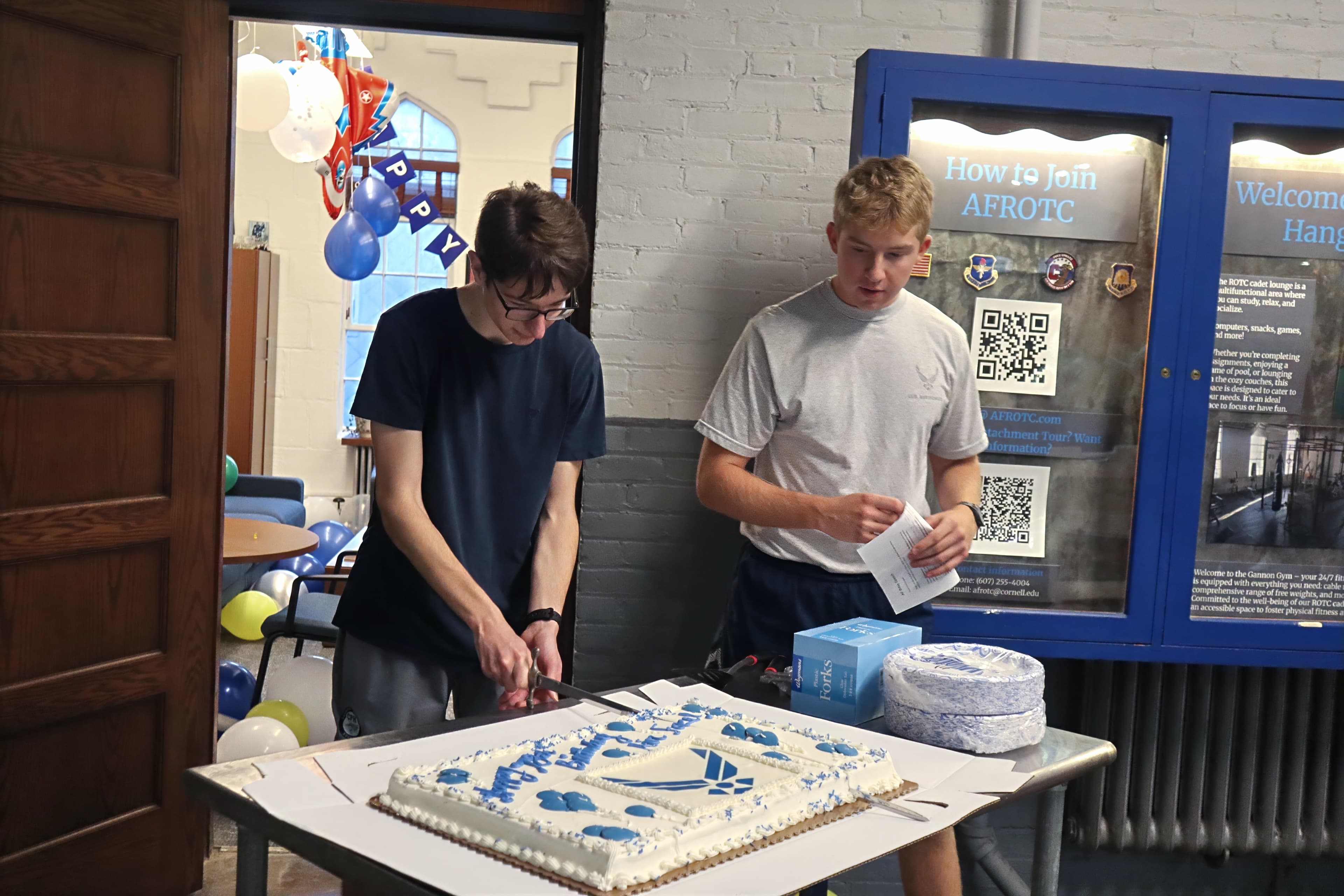 Two cadets cut an Air Force birthday cake with a saber in front of a detachment display case.