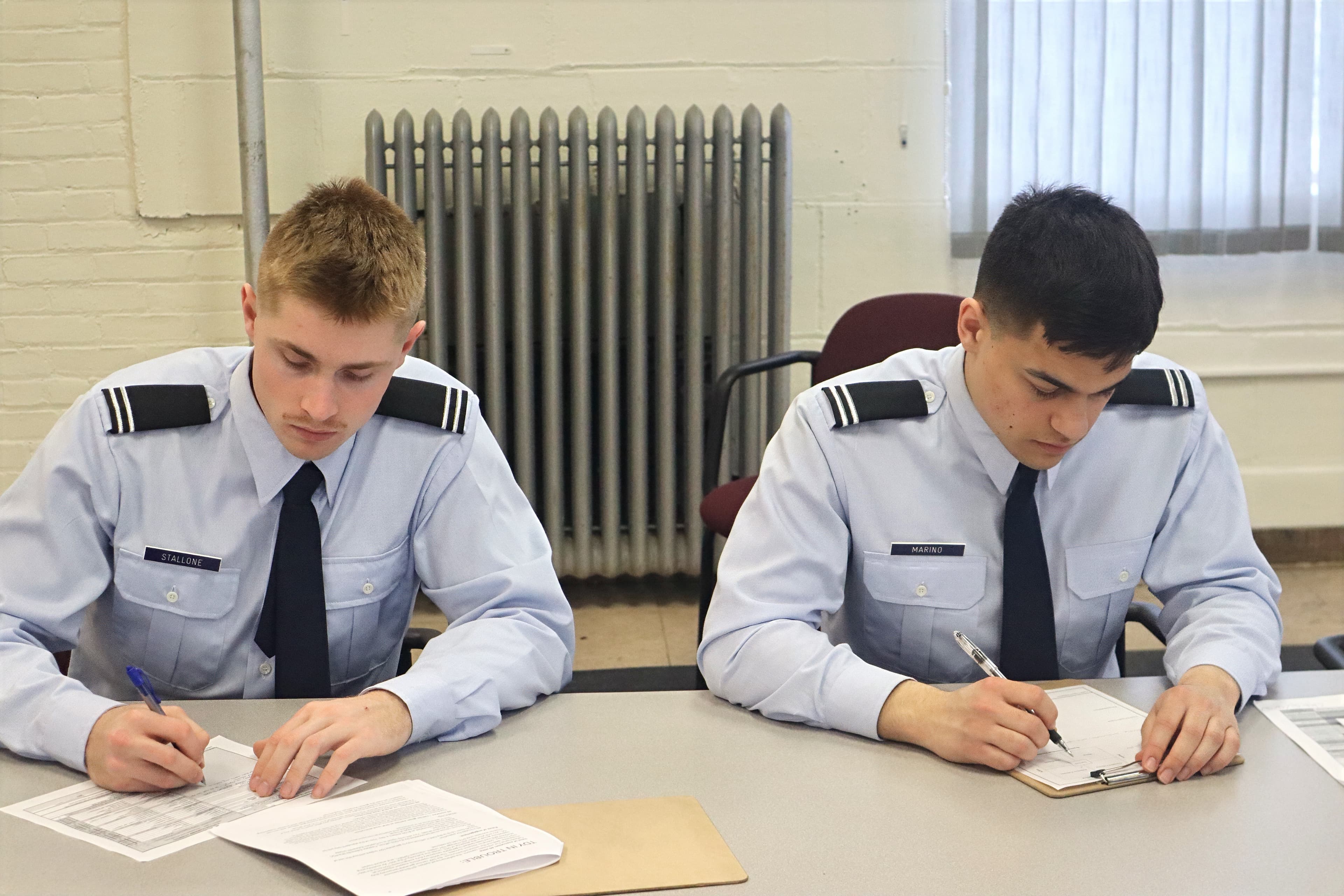 Two cadets in service dress work through paperwork at detachment desks.
