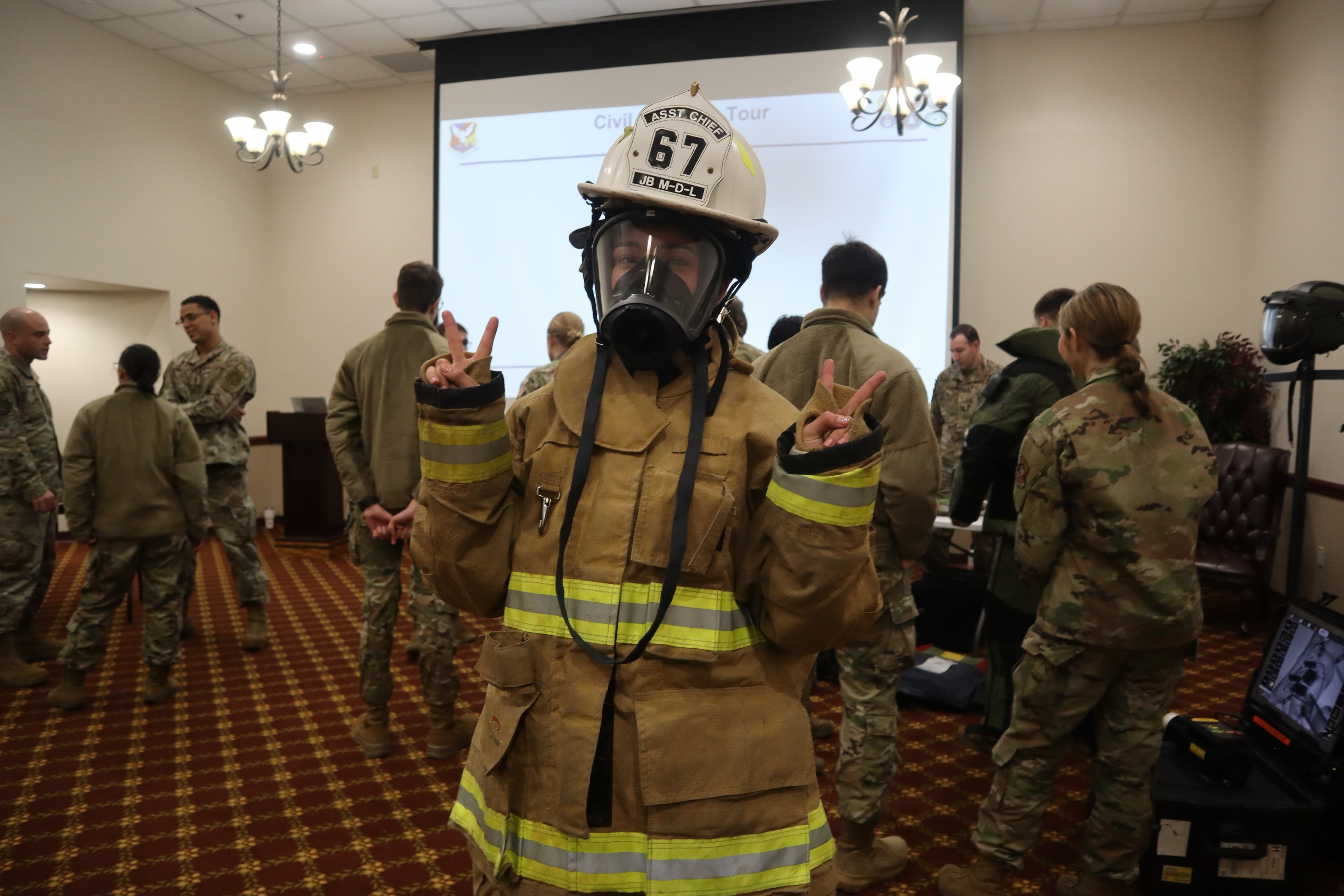 A cadet in firefighting gear gives peace signs during a fire-protection demonstration.