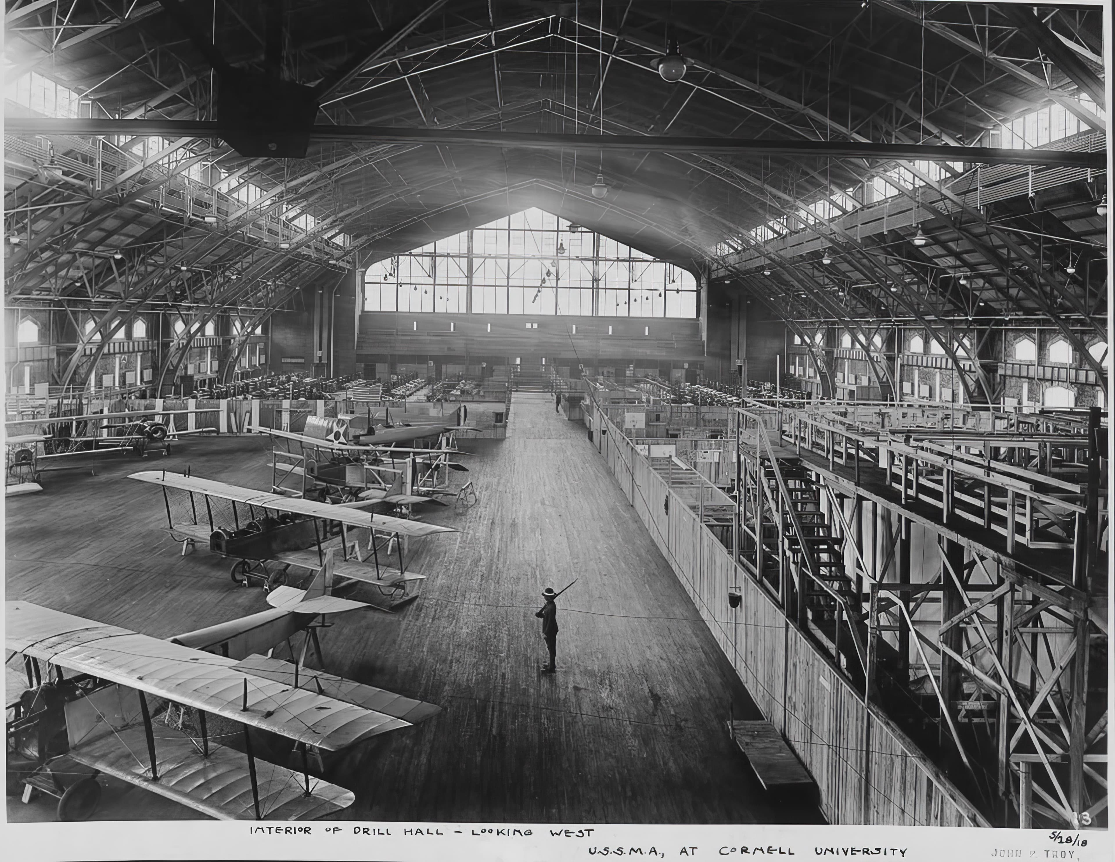 A period photograph captioned Interior of Drill Hall Looking West, U.S.S.M.A. at Cornell University, with biplanes on the floor.
