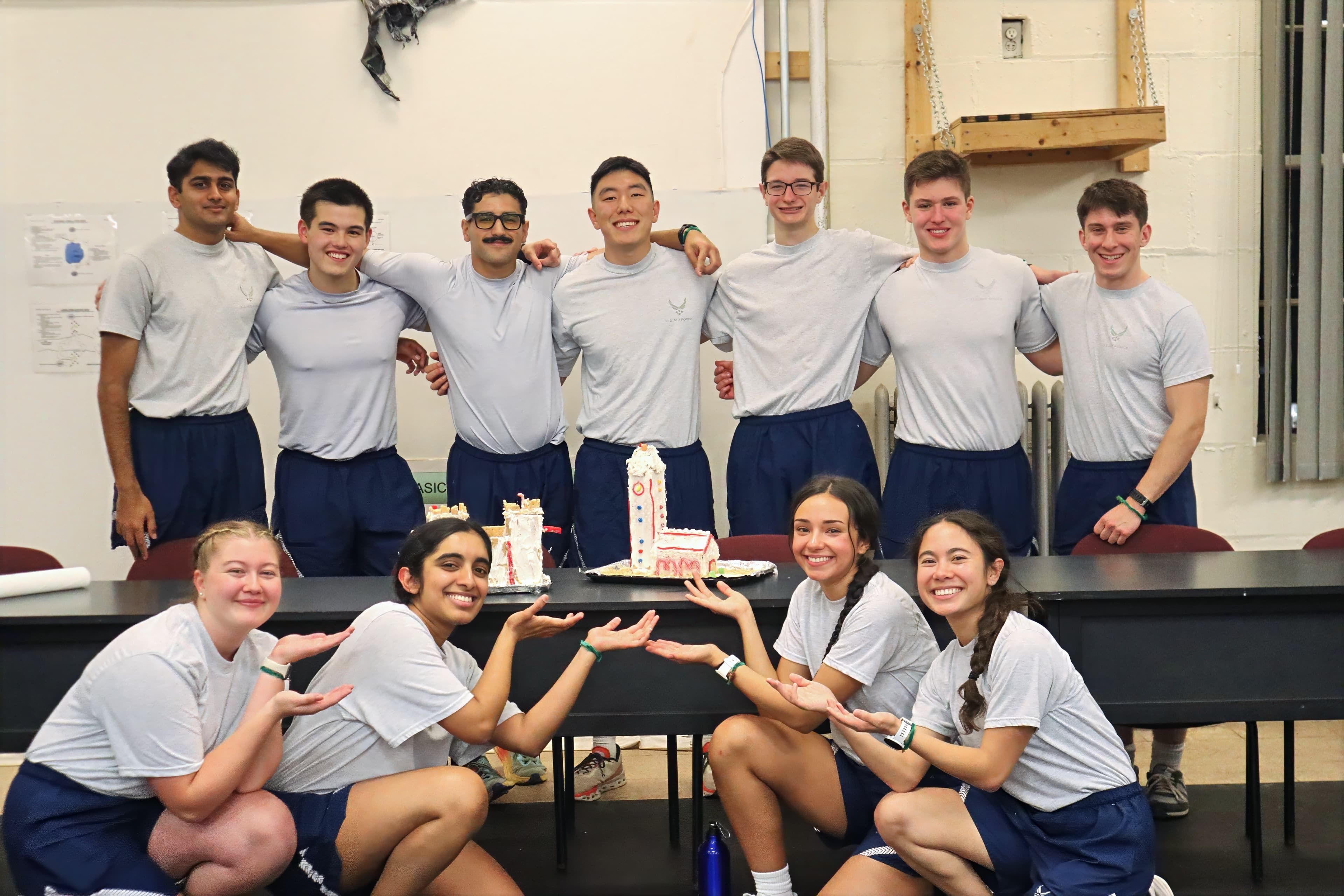 Cadets in physical training gear pose around a cake model of a Cornell clock tower.