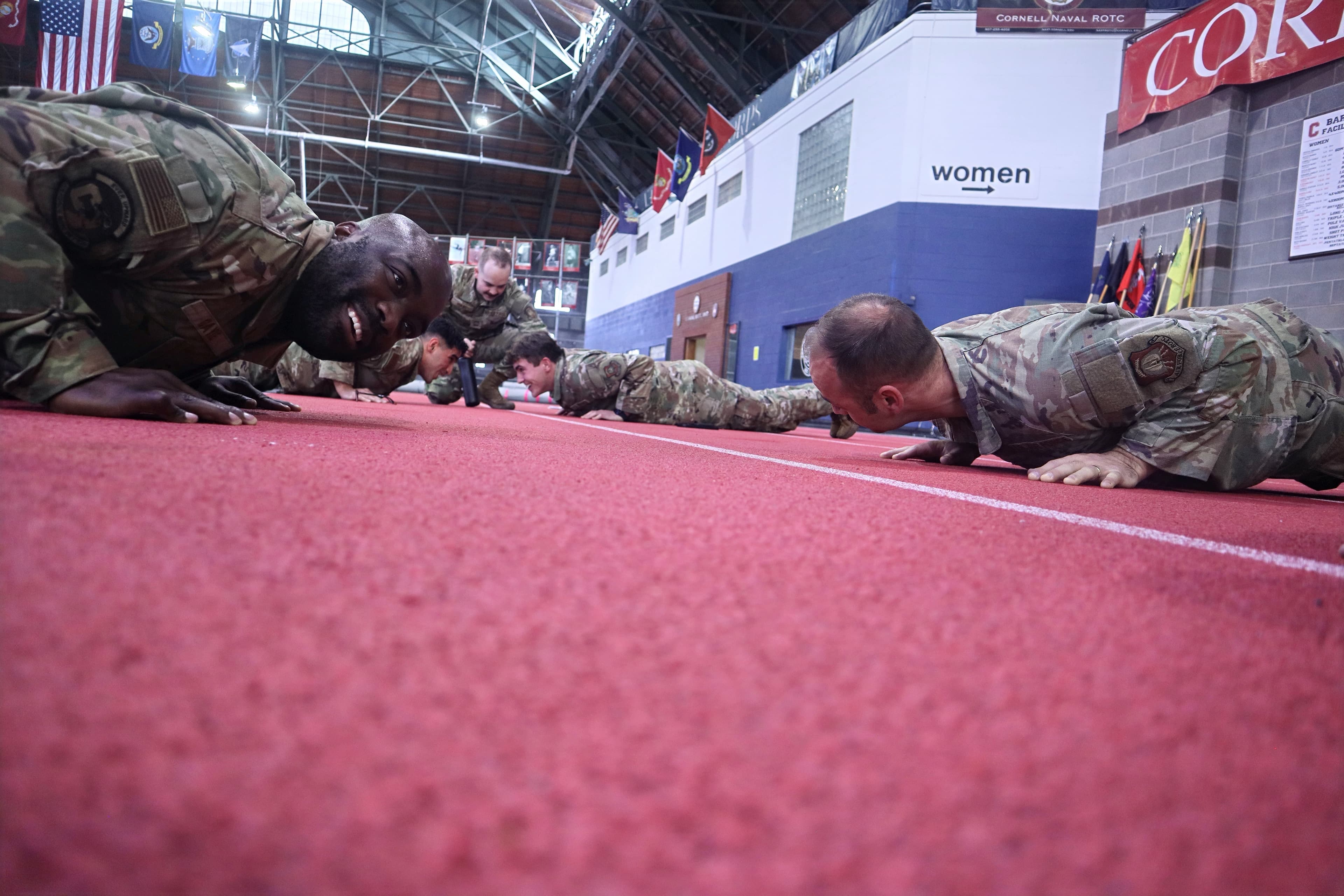 Cadre members do pushups on the track alongside cadets at a low angle.
