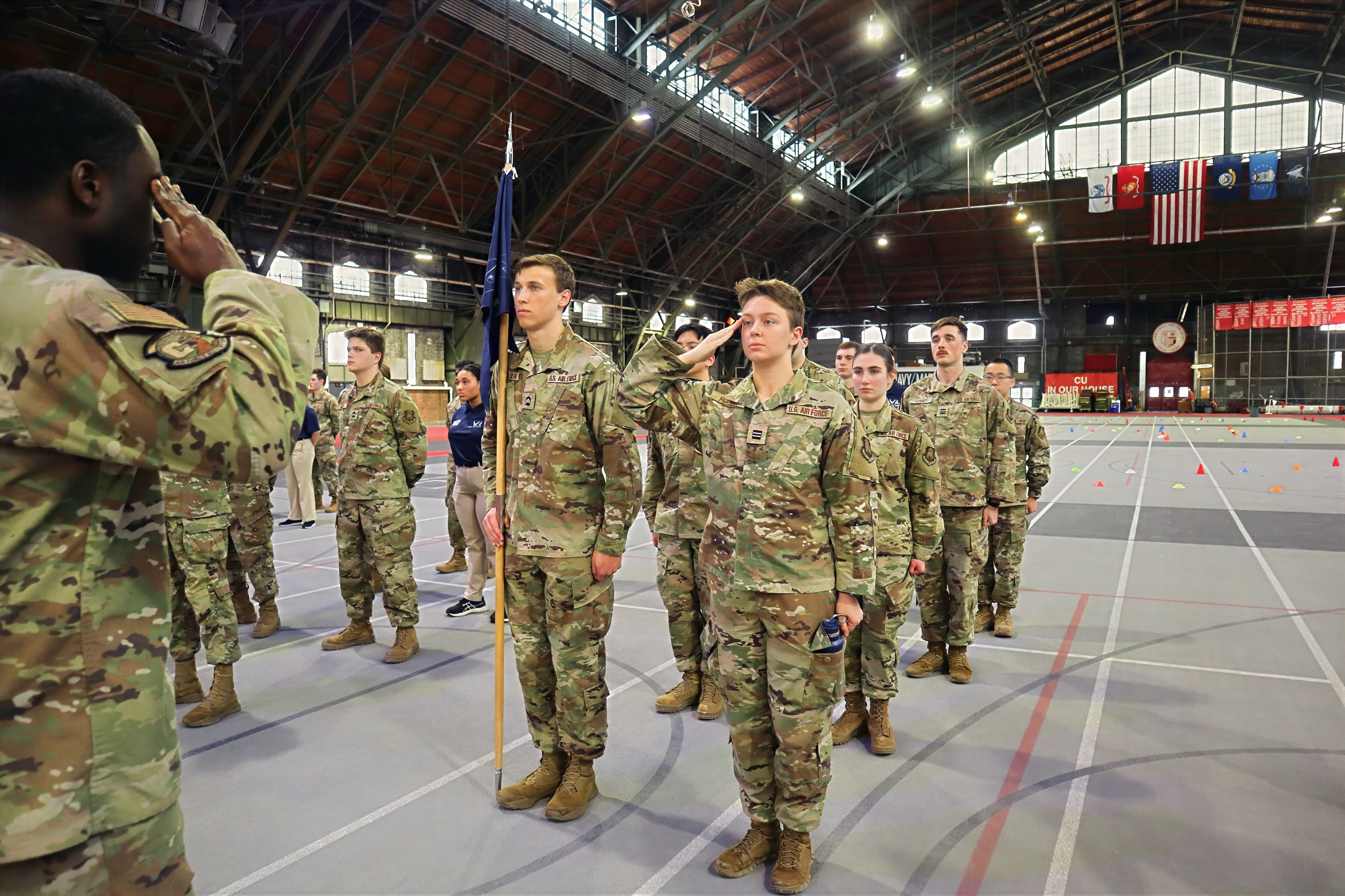 A cadet salutes during a drill evaluation while a flight watches.