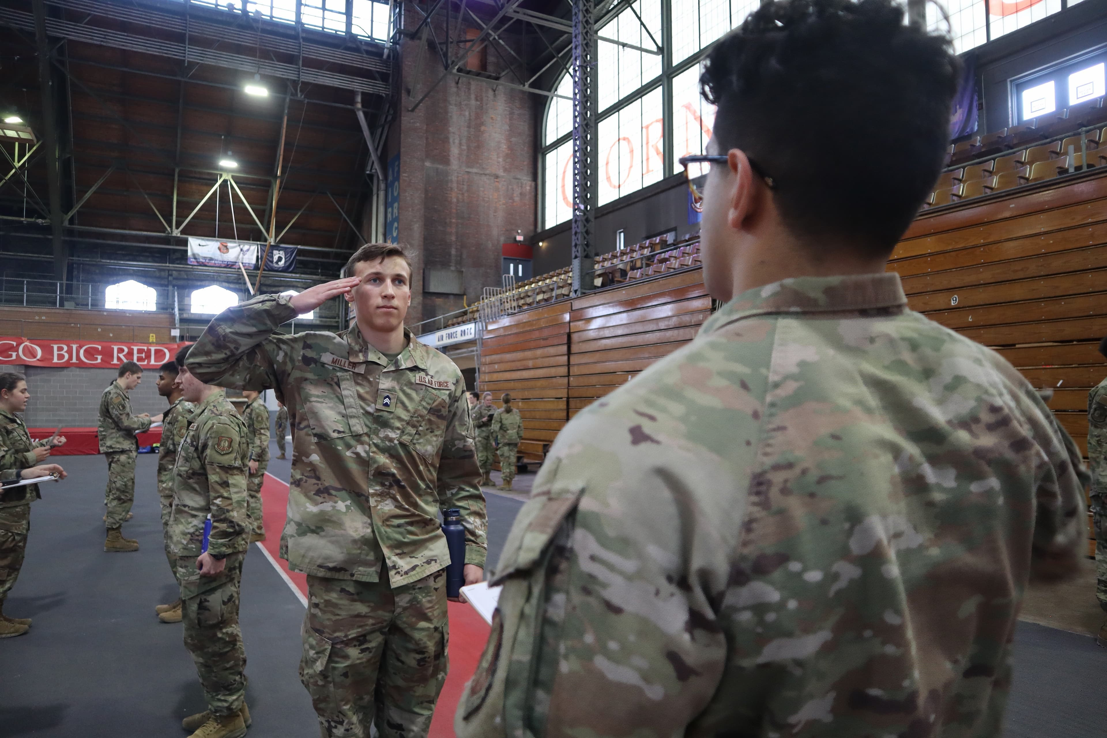 A cadet in service dress salutes at a doorway during door-check training in Barton Hall.