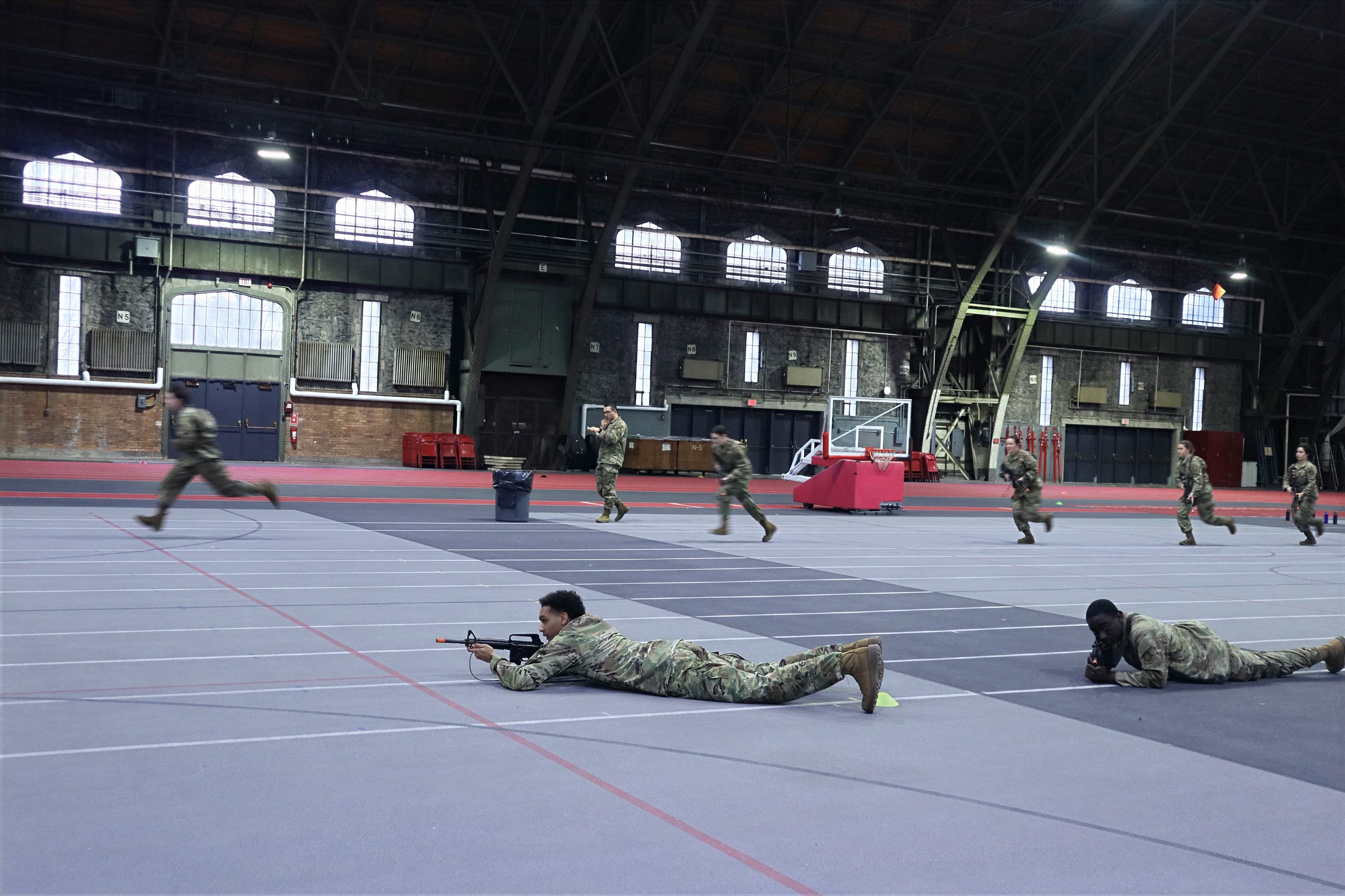 Cadets with training rifles practice small-unit movement across the Barton Hall floor.