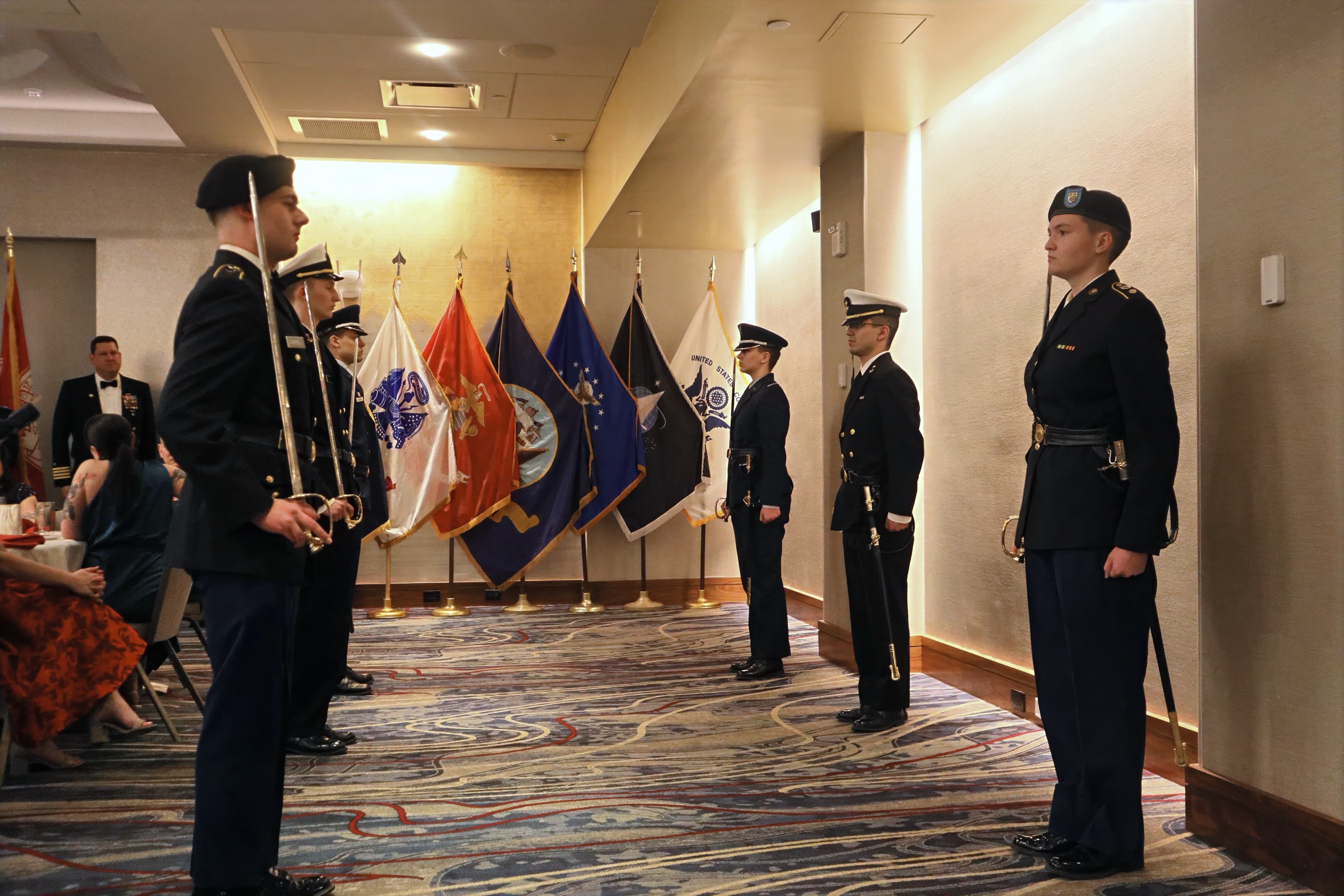 Color guard members prepare flags and sabers in a ballroom before a ceremony.