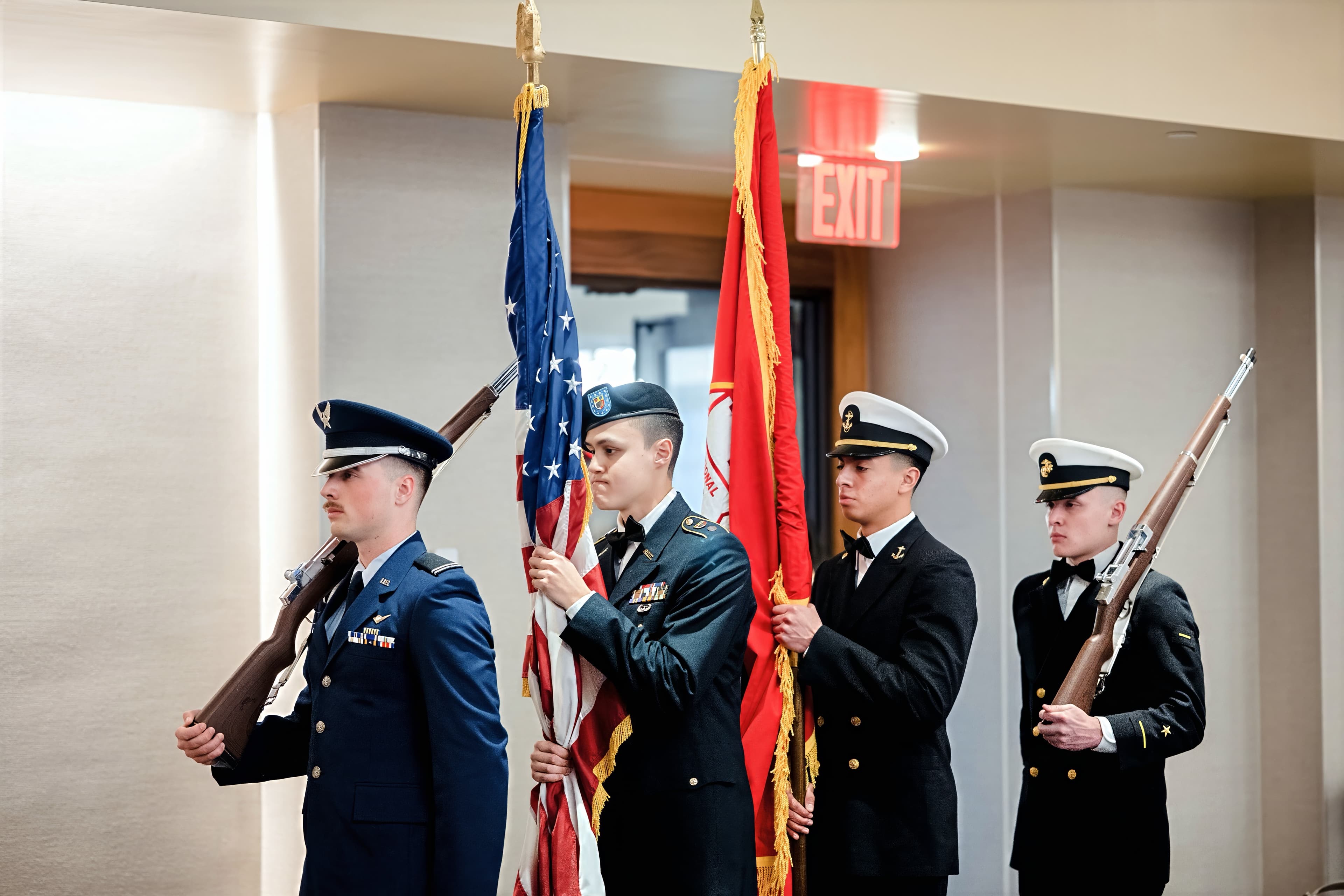 The joint color guard stands posted with flags and rifles at a formal event.