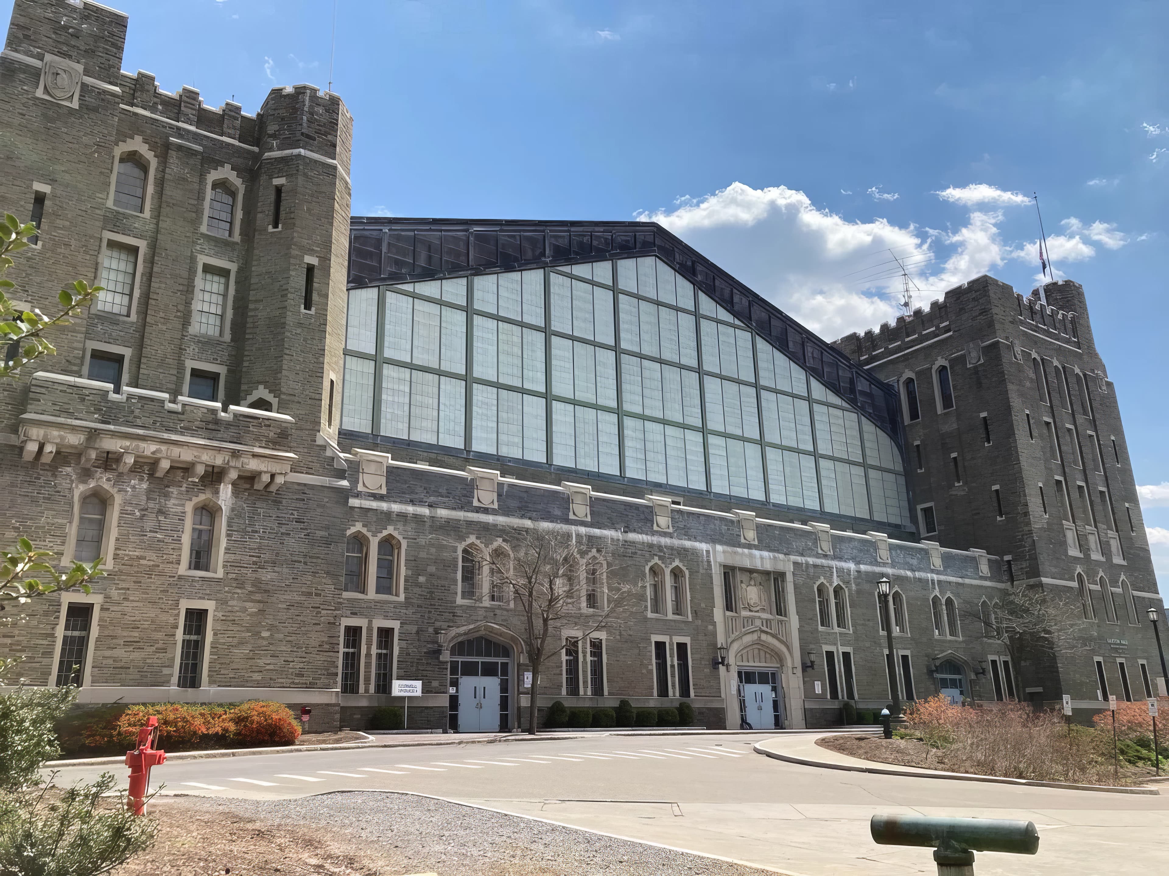 The front of Barton Hall on a clear day, its stone towers flanking the long glass clerestory above the entrance doors.