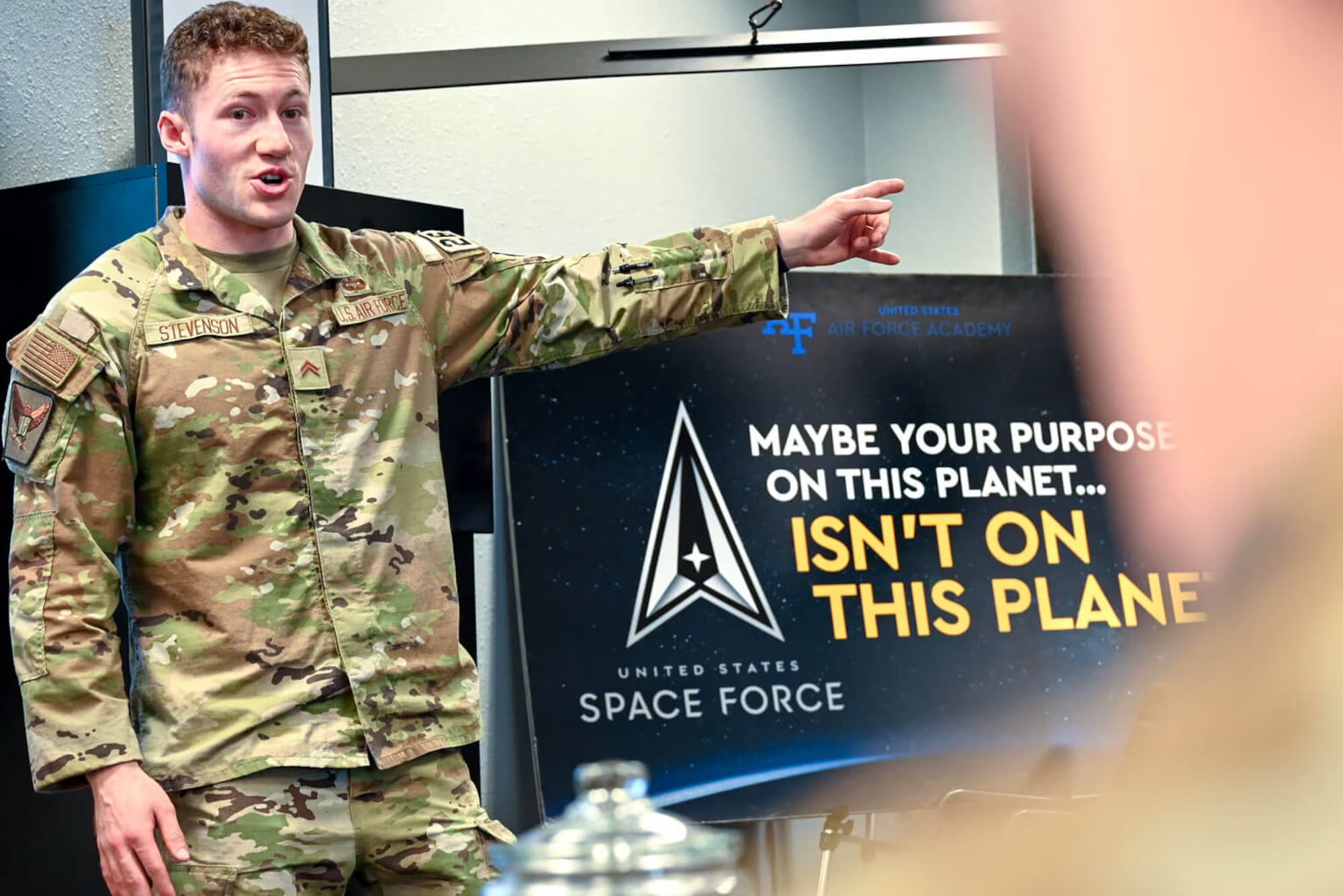 An Air Force Academy cadet gestures toward a United States Space Force recruiting slide while briefing ROTC cadets on i5 Space.