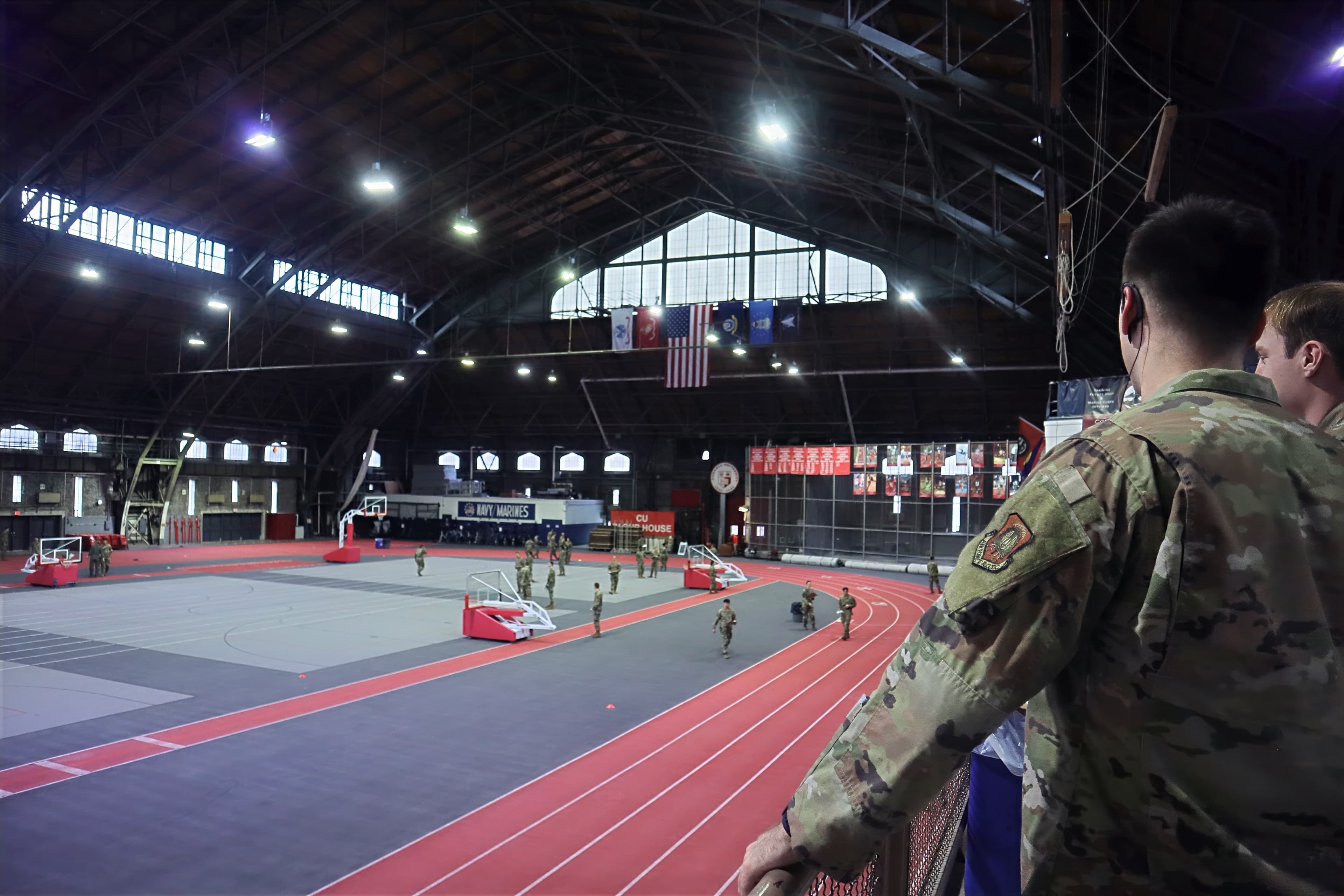 The Barton Hall drill deck seen from the bleachers, with a cadet in the foreground and the indoor track and flags below.